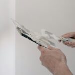 Crop unrecognizable male worker holding metal putty knives while working in room at home